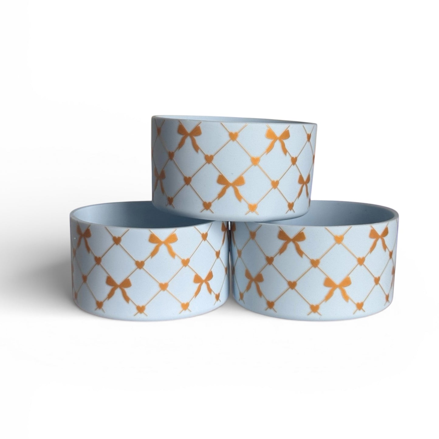 Next Nirvana silicone tumbler boot featuring a light blue base with a gold criss-cross bow and heart pattern.