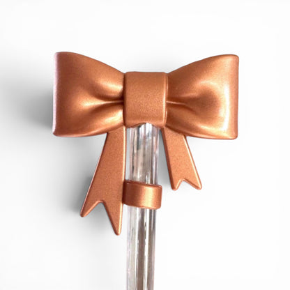 Next Nirvana bronze 3D bow silicone straw topper for tumblers on a clear straw against a white background