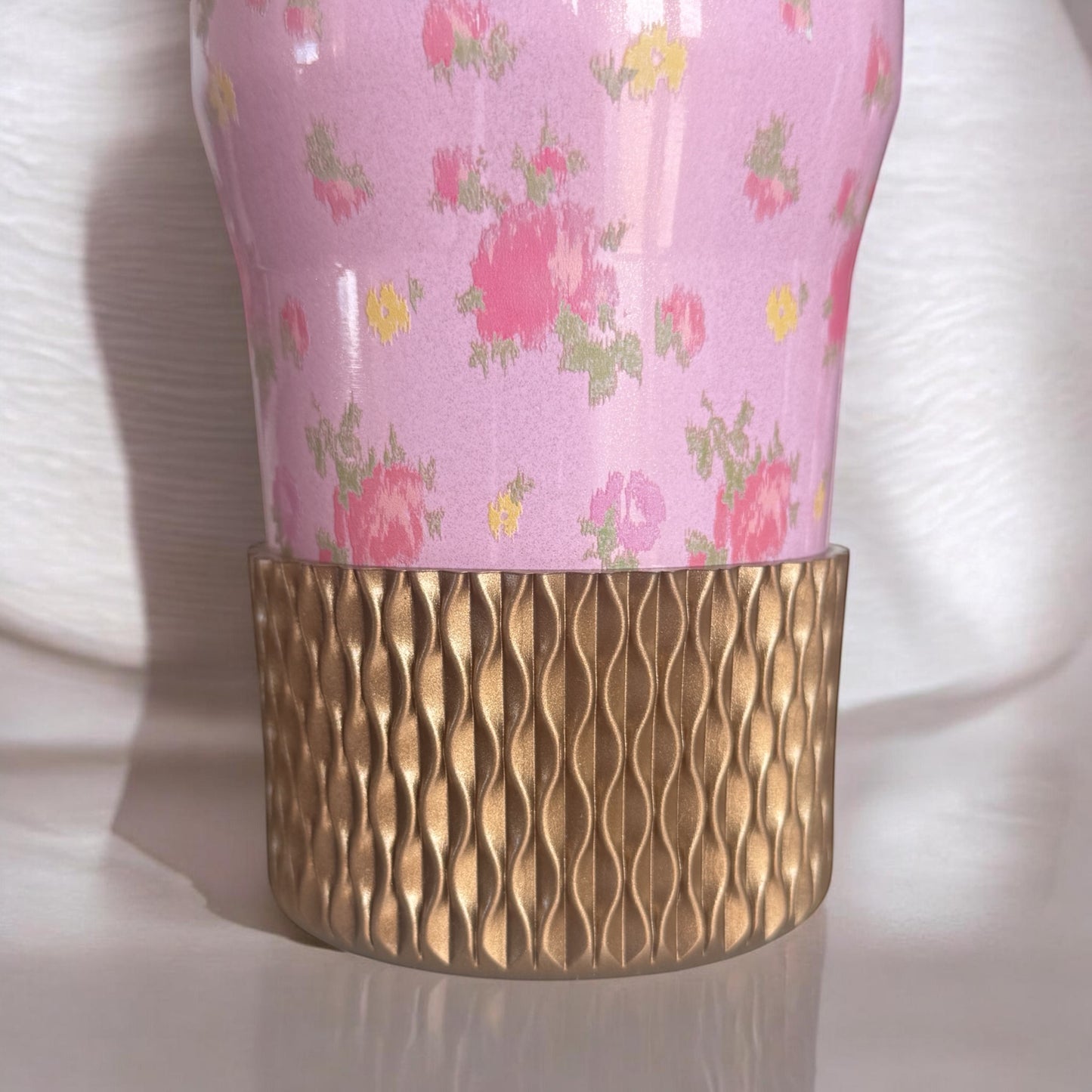 Next Nirvana champagne gold silicone tumbler boot with a 3D textured wave pattern on a floral pink insulated cup.